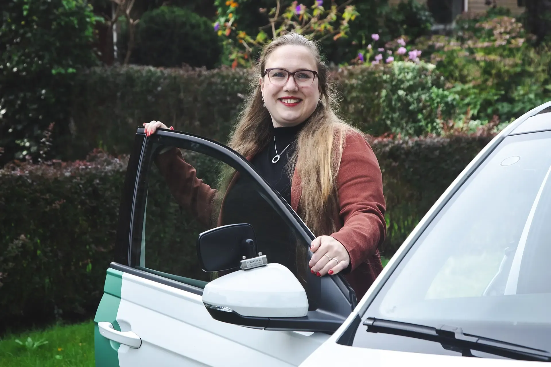 Vrouw glimlachend terwijl ze een autodeur opent.