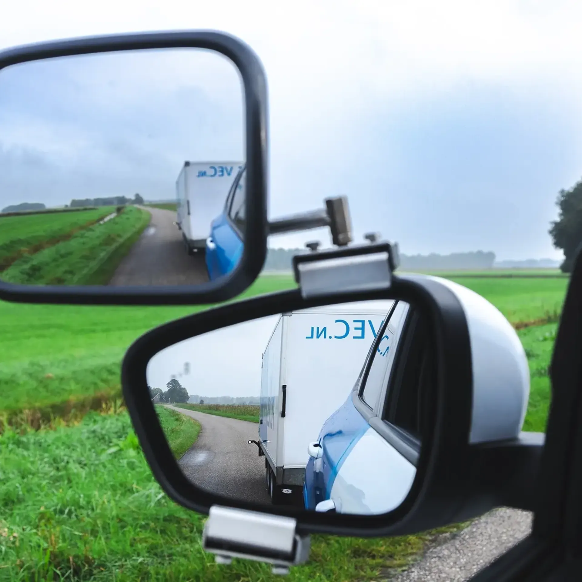 Autospiegel met zicht op groen landschap en weg.